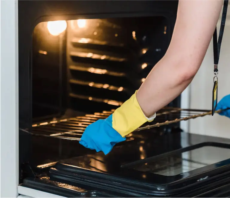 A person cleaning an oven with blue gloves