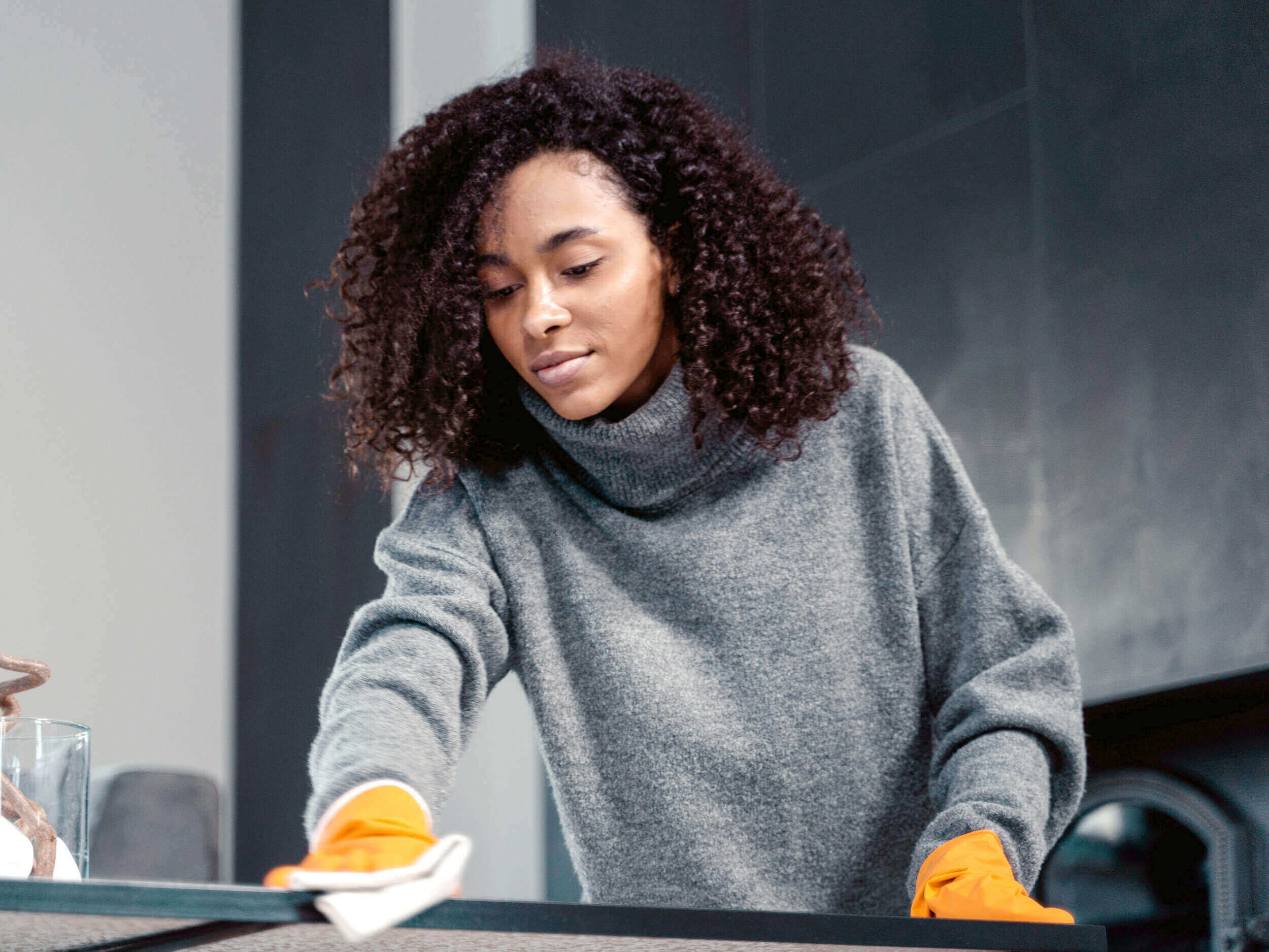 A woman in a gray sweater is cleaning a table
